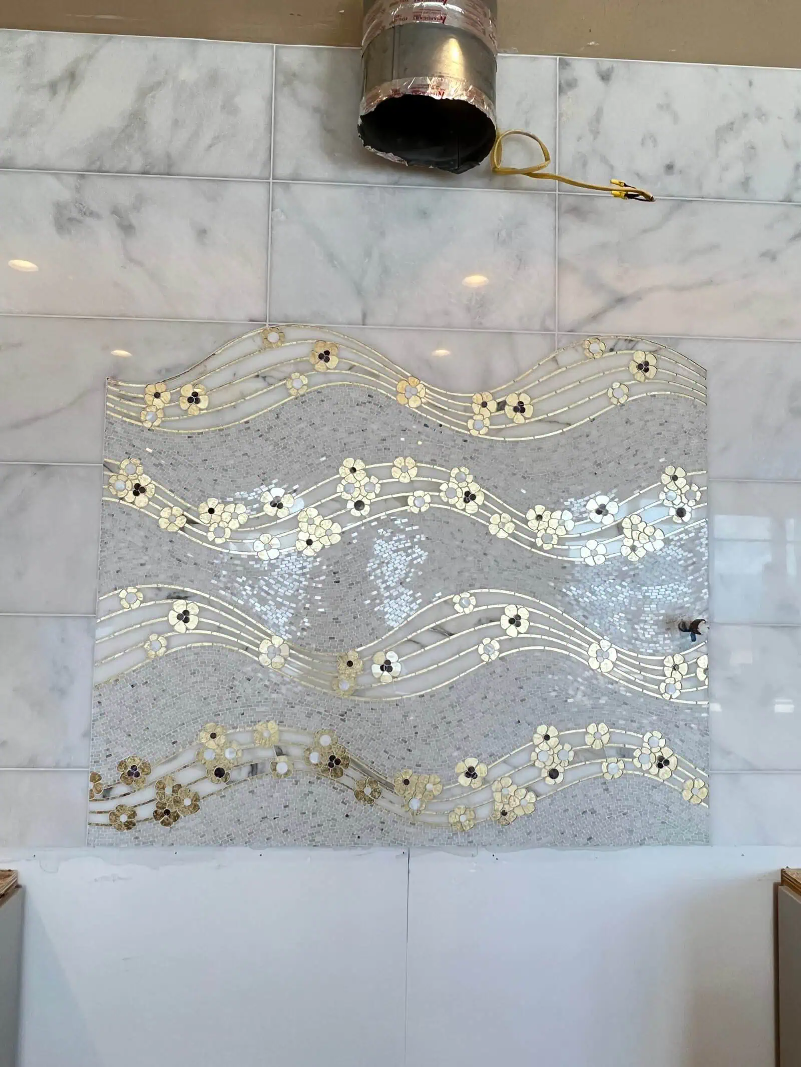 Decorative mosaic tile wall with floral and wave patterns in a modern interior setting.