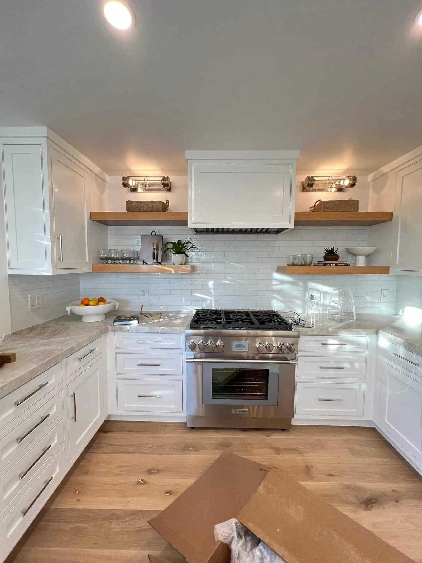 White kitchen with stainless steel stove, white cabinets, and wooden open shelves.