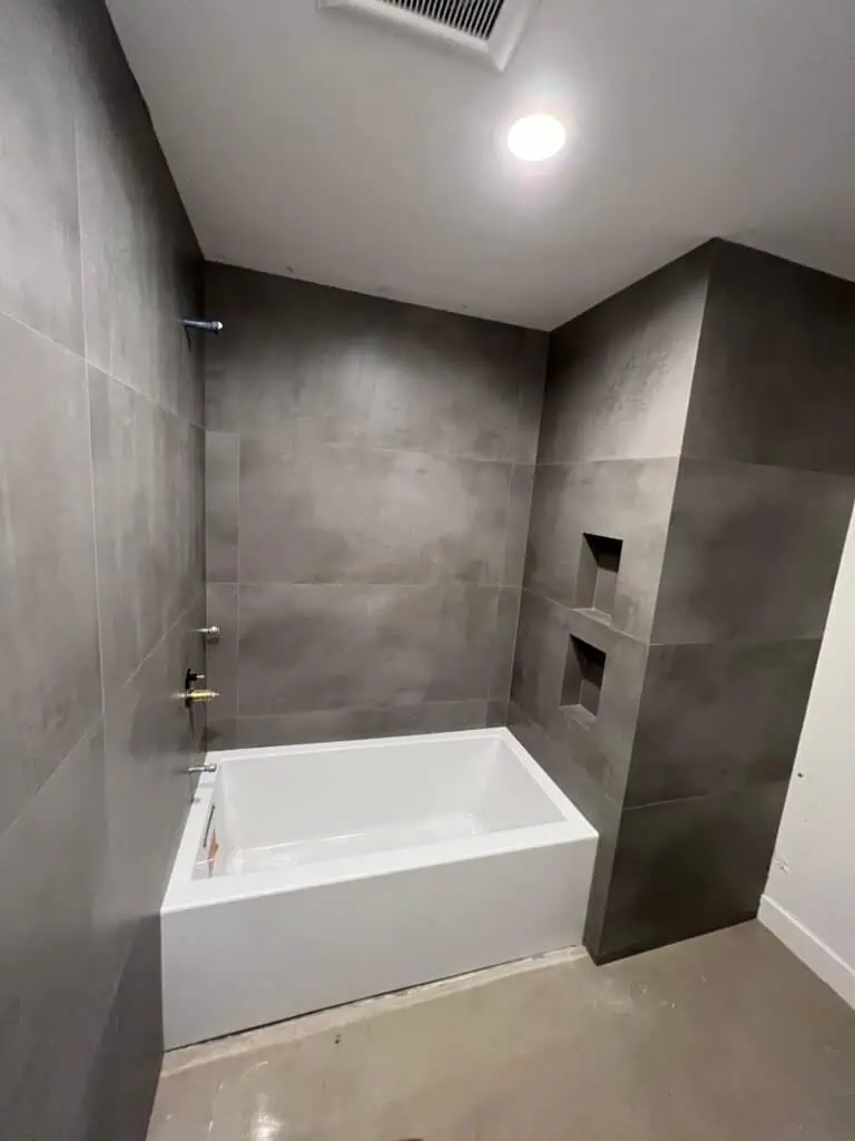 Gray tile bathroom with built-in niches and a white bathtub.
