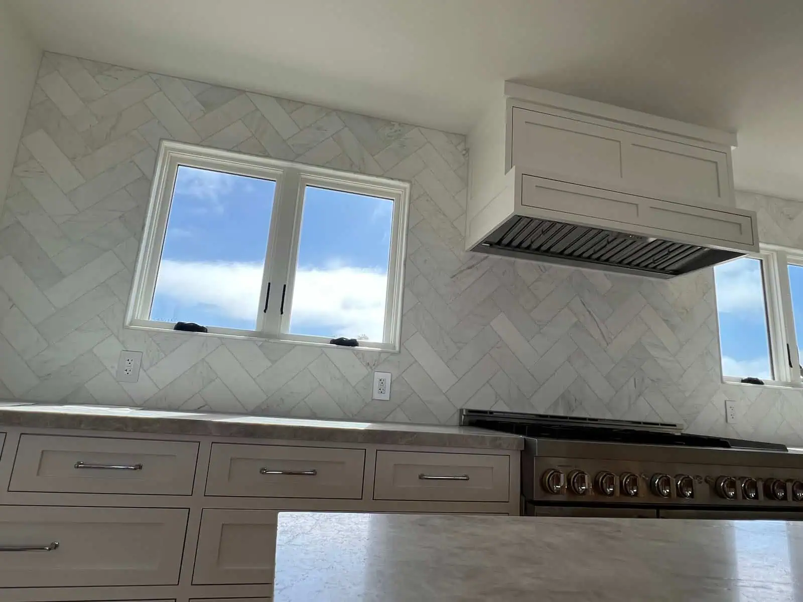 Modern kitchen with white marble geometric wall tiles and stainless steel appliances.